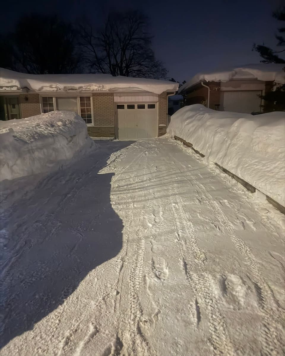 Driveway cleared between snowbanks taller than the garage door after lake-effect snow